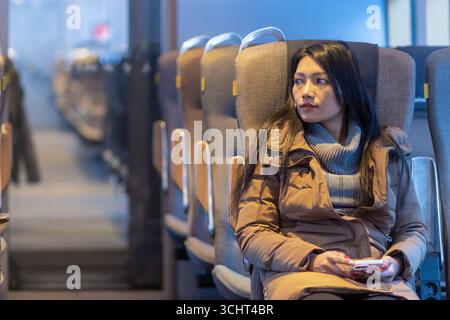 A young woman in winter clothes sits in an train Stock Photo