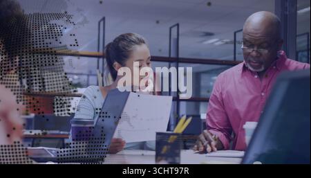 Man in pink shirt pointing with woman in blue top listening at office desk, digital overlay Stock Photo