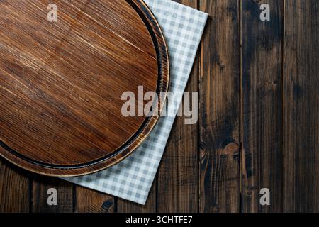 Empty board for pizza over napkin on wooden kitchen table, top view, close up, copy space Stock Photo