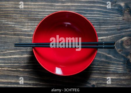 A pair of black chopsticks lying across an empty red soup bowl on wooden table, close up, top view Stock Photo