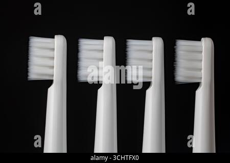 Four white plastic toothbrushes on a black background, close up Stock Photo