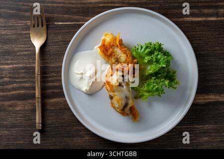 Two delicious cabbage rolls stuffed with meat and rice on a plate along with sour cream and lettuce, close up, top view Stock Photo