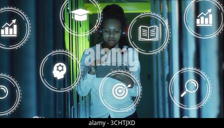 Tech professional woman tapping tablet in server rack corridor, showing floating analytics icons Stock Photo
