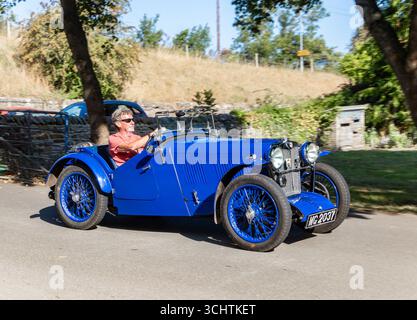 a man  enjoying a drive in a 1930s vintage blue convertible MG J2 Midget car on a sunny day with countryside scenery in the background Stock Photo