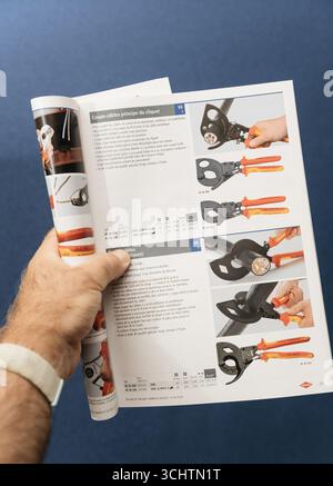 Paris, France - Aug 4, 2025: Hand holding open catalog showing detailed product listings and images of ratchet cable cutters for professional electric Stock Photo
