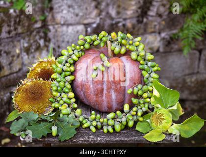 Beautiful earthy autumn composition with a pumpkin decorated with a handmade green acorn garland and golden sunflowers. Vintage floral arrangement Stock Photo
