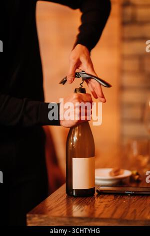 Close-up of hands opening wine bottle with corkscrew in warm, elegant restaurant atmosphere Stock Photo
