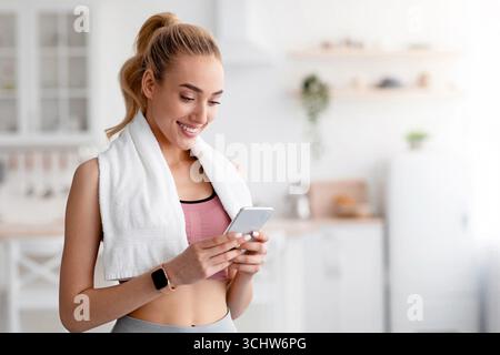 Happy european cute millennial blonde female checking fitness app or social media on smartphone Stock Photo
