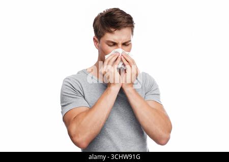 Unhappy millennial european attractive man blows his nose in napkin and suffers from runny nose Stock Photo
