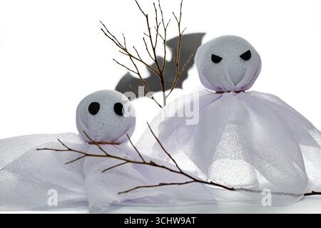 Two ghostly figures made from white mesh fabric stand against a light background, casting mysterious shadows. Twisted branches add an eerie touch to t Stock Photo