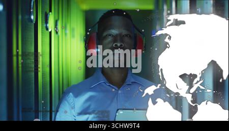 Engineer in blue shirt and red headset monitoring racks in data center, with world map overlay Stock Photo