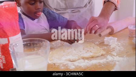 Pressing star-shaped cutter, father and son shaping dough on home kitchen countertop with sprinkles Stock Photo