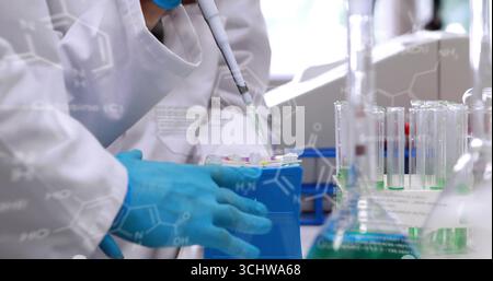 Scientist in lab coat transferring liquid using pipette at bench, with tubes, formulas, copy space Stock Photo