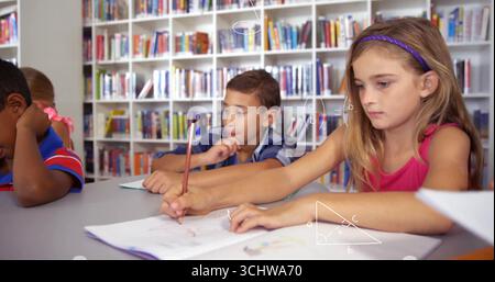 Studying four schoolchildren writing and drawing at gray table in library, with pencils, notebooks Stock Photo