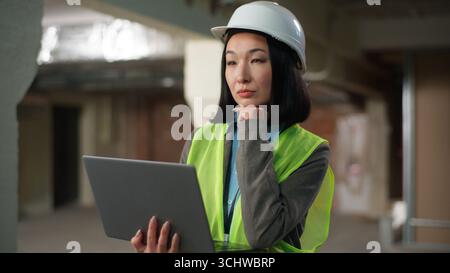 Asian Korean Chinese Japanese woman builder engineer thinking analyzing female using laptop computer typing data building project plan construction Stock Photo
