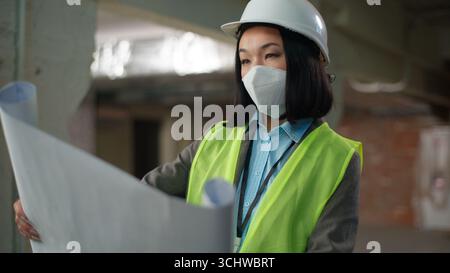 Asian Korean Chinese Japanese woman builder looking check construction plan building project blueprint female inspector girl nod head engineer Stock Photo