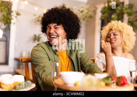 Diverse friends laughing and enjoying snacks at cozy home gathering, feeling joyful, on patio Stock Photo