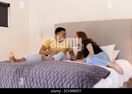 Young diverse couple laughing and talking while relaxing together on bed at home Stock Photo