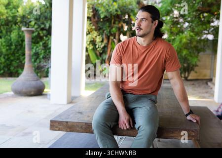 Man sitting on outdoor table, looking away, enjoying peaceful garden view Stock Photo