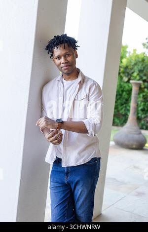 Smiling man in casual outfit standing outdoors, leaning against pillar Stock Photo