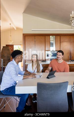 Diverse friends discussing project at home, using tablet and documents on table Stock Photo