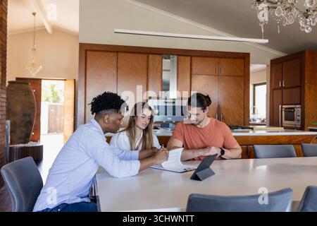 Diverse friends discussing project at home, using tablet and notebook on table Stock Photo