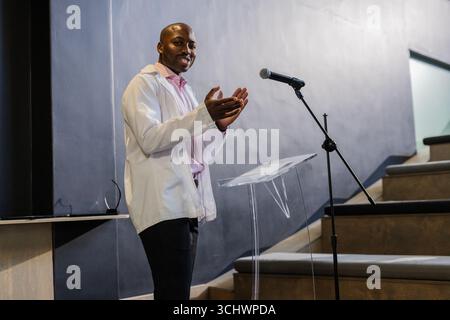Businessman in white jacket clapping while speaking at podium in conference hall Stock Photo