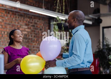 Holding colorful balloons, colleagues in office chatting and celebrating together Stock Photo