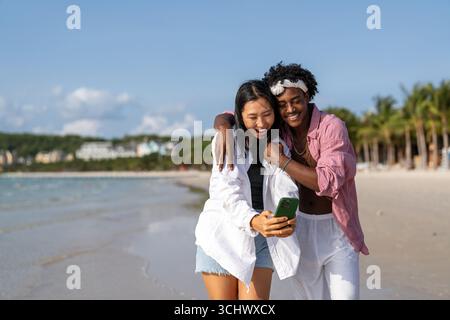 Trendy digital creator couple taking selfie by the beach, sharing travel content for social media Stock Photo
