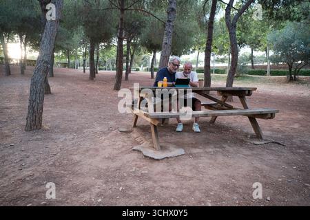 Two senior men using tablet and relaxing at picnic table in park Stock Photo