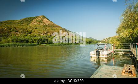 Boat with Georgian flag moored on river dock surrounded by green hills in Mtskheta, Georgia, under clear blue sky Stock Photo