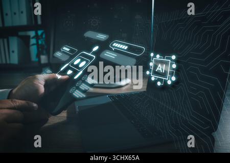 Chatbot conversation and artificial intelligence concept, with a hand holding smartphone showing glowing AI icons beside laptop in digital workspace Stock Photo