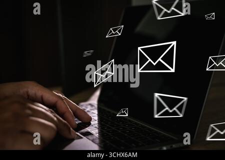 Close-up of hands typing on laptop keyboard with floating email icons, concept of digital communication, online messaging, email marketing, and intern Stock Photo