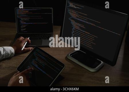 Programmer pointing at laptop screen with visible lines of code and tablet beside, concept of coding, software development, IT, cybersecurity, and dig Stock Photo