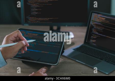 Close-up of programmer freelance working on tablet and laptop with code on screen, modern software development, coding, and remote work in home office Stock Photo