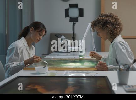 Expert conservators team working in the laboratory, they are cleaning an oil painting using cotton swabs Stock Photo