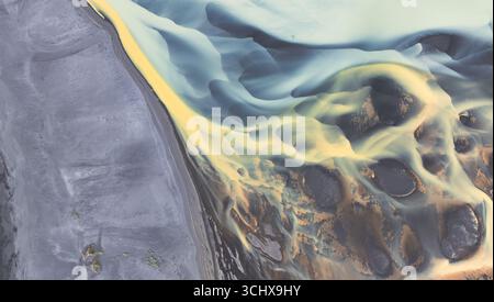 Aerial view of swirling glacial rivers carve through the volcanic landscape, creating ethereal patterns of gold and grey, Hvolsvllur, Southern Region, Stock Photo