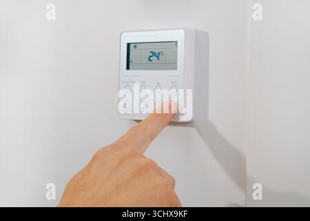 close-up of a man pressing the power button of an air conditioning display mounted on a white wall, turning the appliance on or off at 24 degrees cels Stock Photo