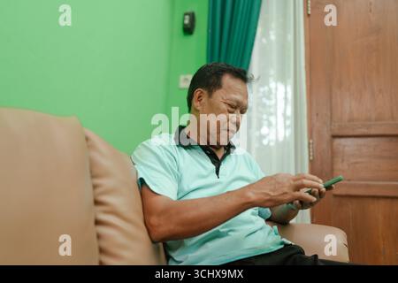 An elderly man enjoys using his smartphone in a cozy, welllit living room Stock Photo