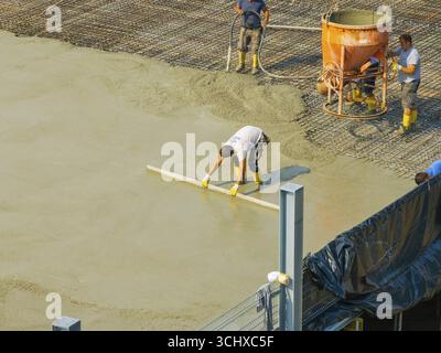 Workers smoothing concrete on a construction site while a concrete mixer stands in the background, car park construction, Calw, Germany Stock Photo