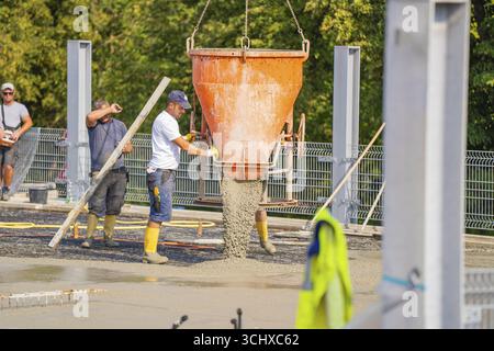 Two workers pouring concrete from large mixer tubs, surrounded by safety measures and mesh fencing, car park construction, Calw, Germany Stock Photo