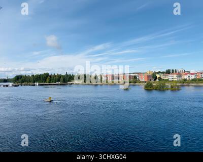 Scenic view of a blue river with trees and buildings under a bright sky. Stock Photo