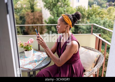 Woman drinking coffee and using mobile phone at home balcony Stock Photo