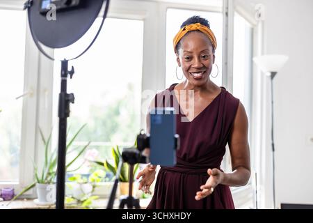 Smiling beautiful woman vlogging using her mobile phone at home Stock Photo