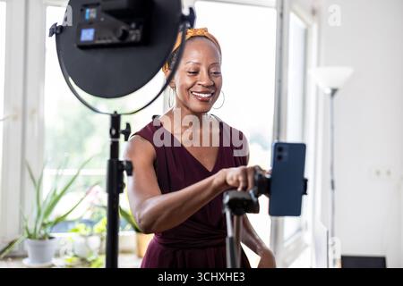 Smiling beautiful woman vlogging using her mobile phone at home Stock Photo