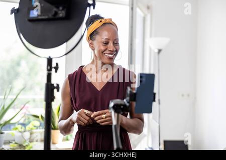 Smiling beautiful woman vlogging using her mobile phone at home Stock Photo