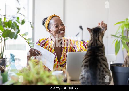 Portrait of smiling woman working on laptop with cat on her desk Stock Photo