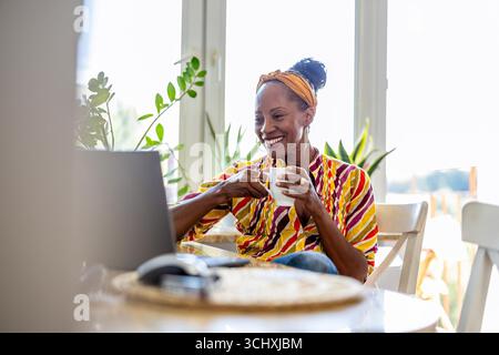 Happy woman drinking coffee and using laptop at home Stock Photo
