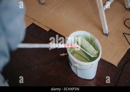 Close-up of a paint roller in a bucket of green paint, set on a dark wooden floor during a room renovation process Stock Photo