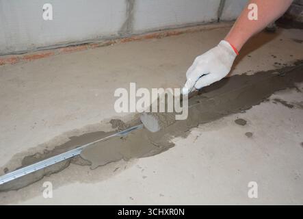 The builder covers the aluminum beacons with cement mortar for subsequent pouring of the floor with concrete. Stock Photo